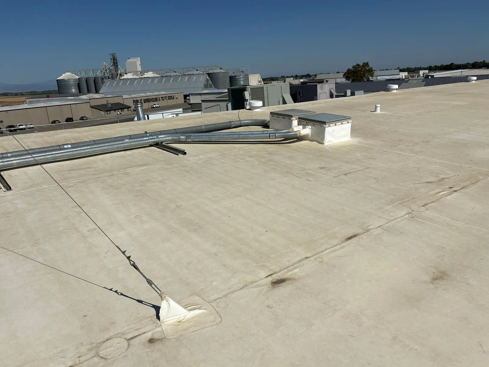 A white commercial flat roof outside Chico with grain silos in the background, typical of North Valley ag buildings