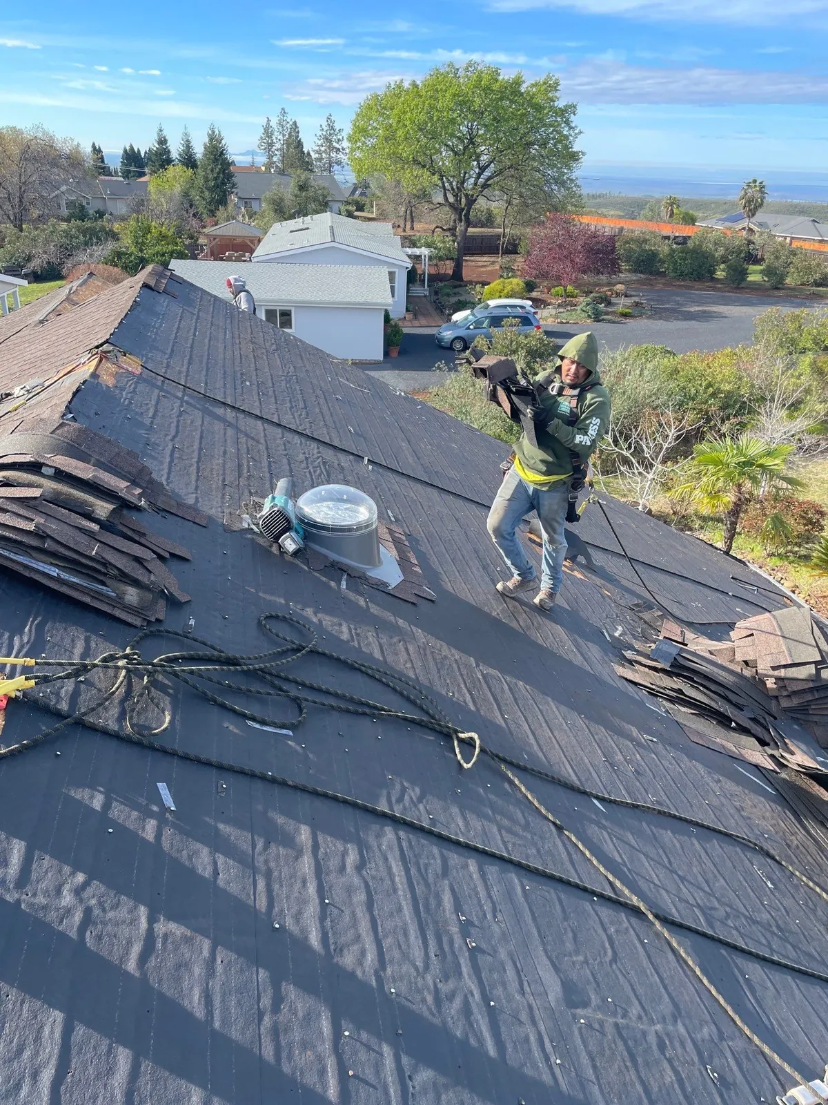 Butte Roofing crew member carrying new shingles across a Chico roof stripped to the underlayment after wind damage