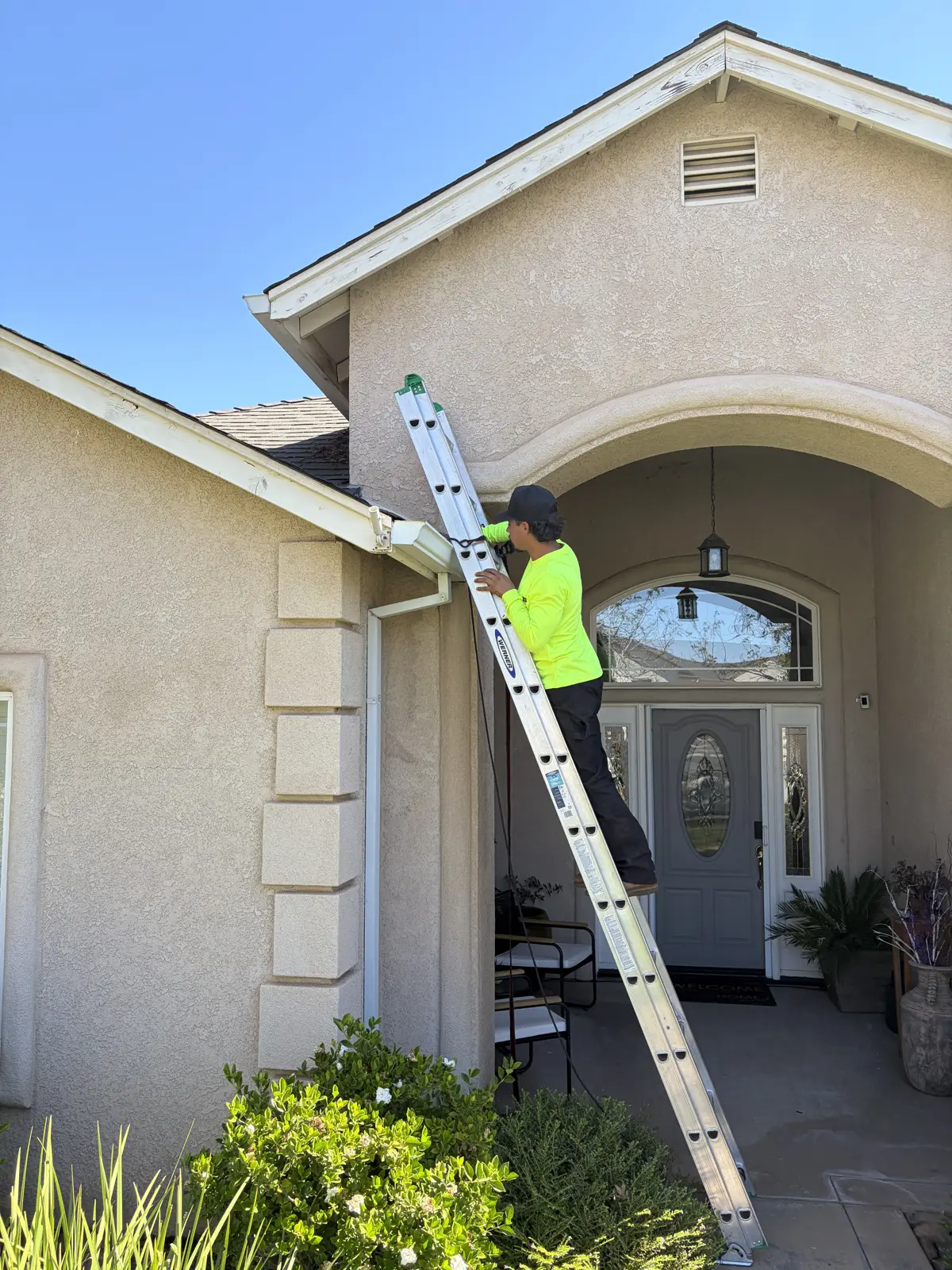 Butte Roofing technician on a ladder cleaning a residential gutter in Chico, CA